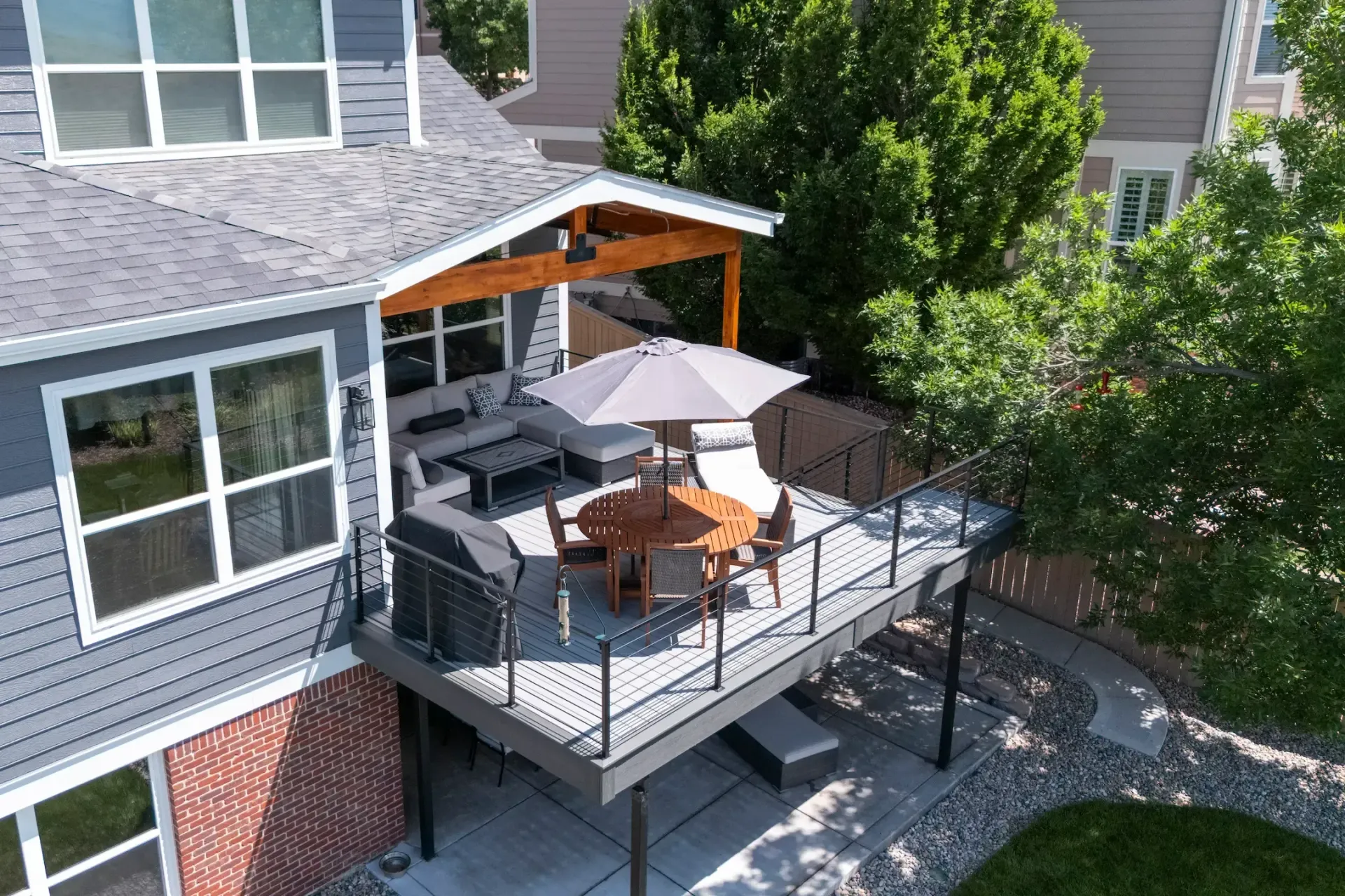 Backyard deck with outdoor dining table, umbrella, grill, and gray house exterior