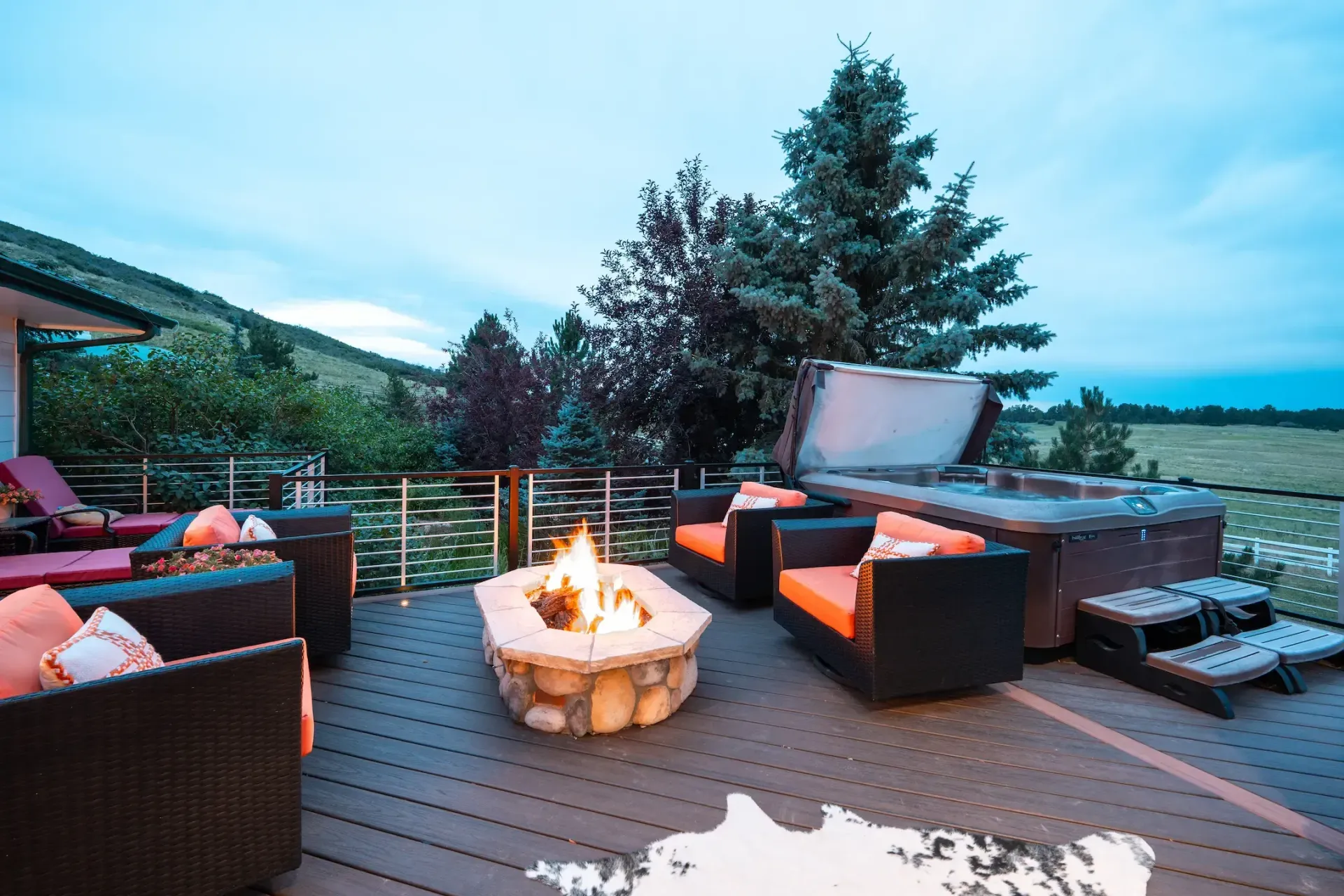Patio lounge with fire pit, wicker seating, and mountain lake view at dusk