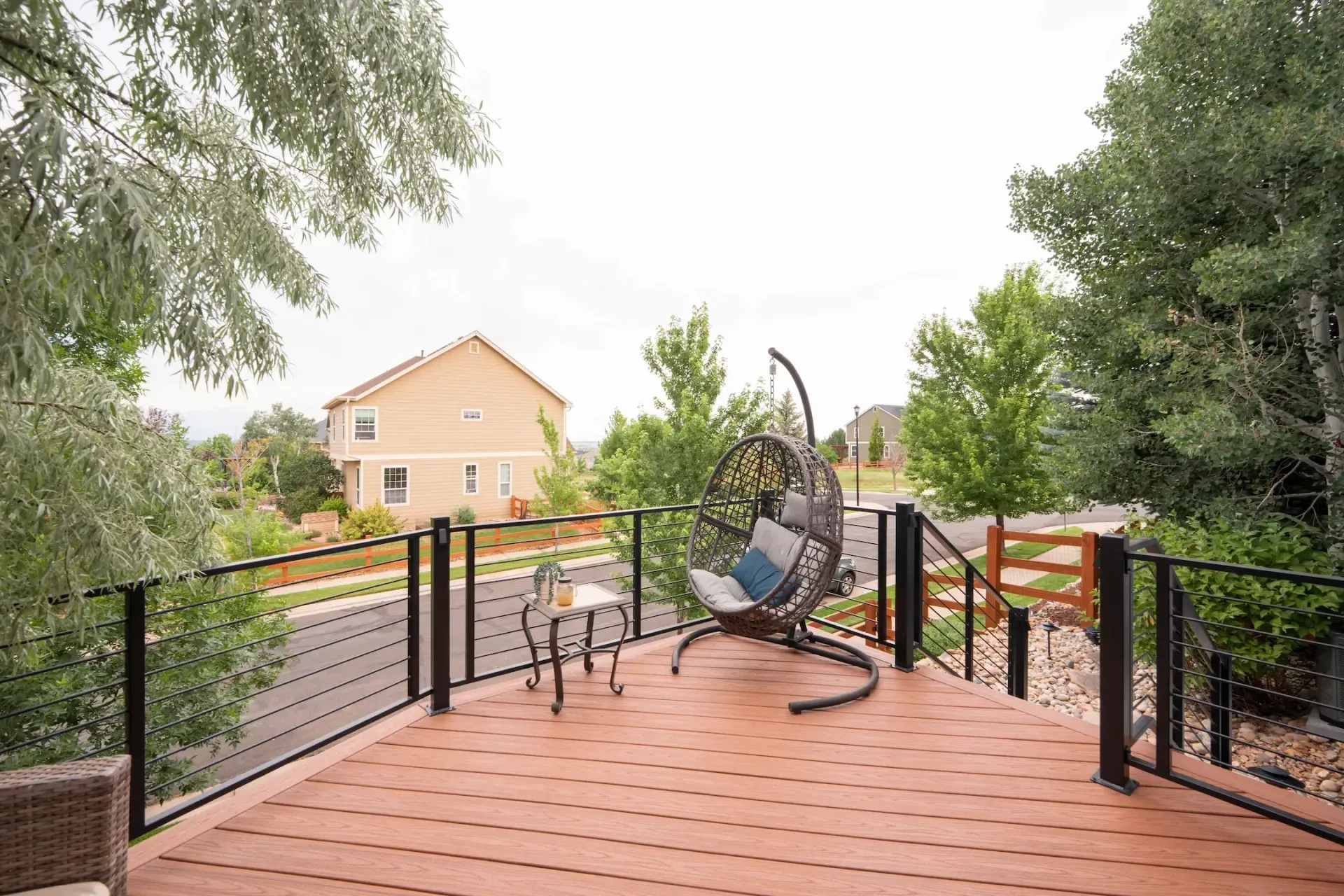 Backyard deck with railings and outdoor furniture, overlooking a yard and house beyond.