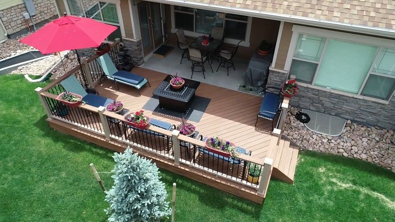 Backyard deck with patio furniture, red umbrella, and fenced lawn beside a house