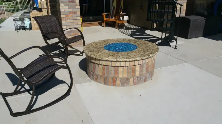 Outdoor brick fire pit with blue cap, surrounded by black rocking chairs on a patio