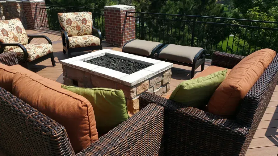 Outdoor patio seating with woven chairs and benches around a rectangular fire pit on a deck.