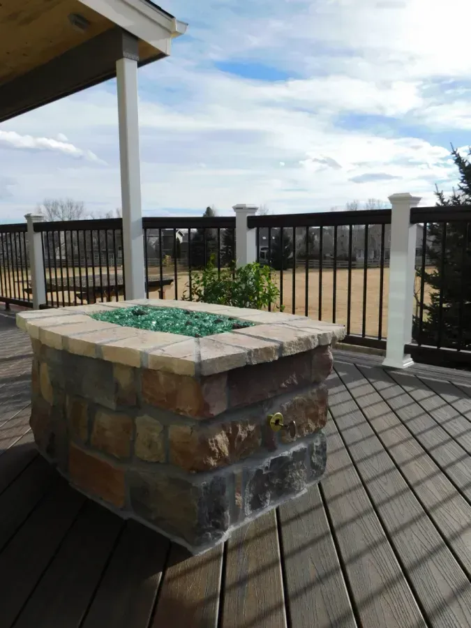 Stone outdoor fire pit on a tiled patio with railing and open sky view