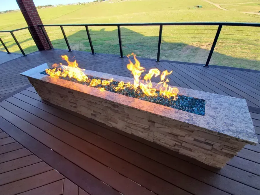 Modern deck with long stone fire pit burning on a patio overlooking a green field