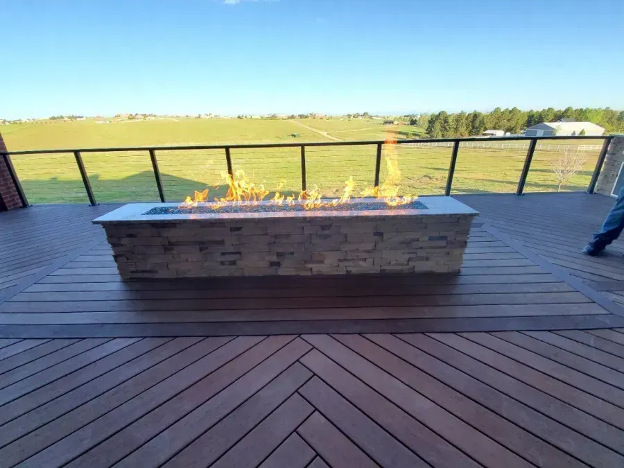 Outdoor deck with a long stone fire table overlooking a grassy field and blue sky