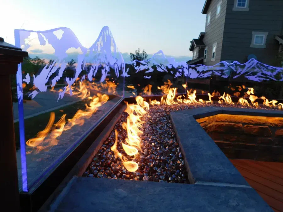 Modern backyard fire feature with flames along a gravel-lined path at dusk, mountains in the background