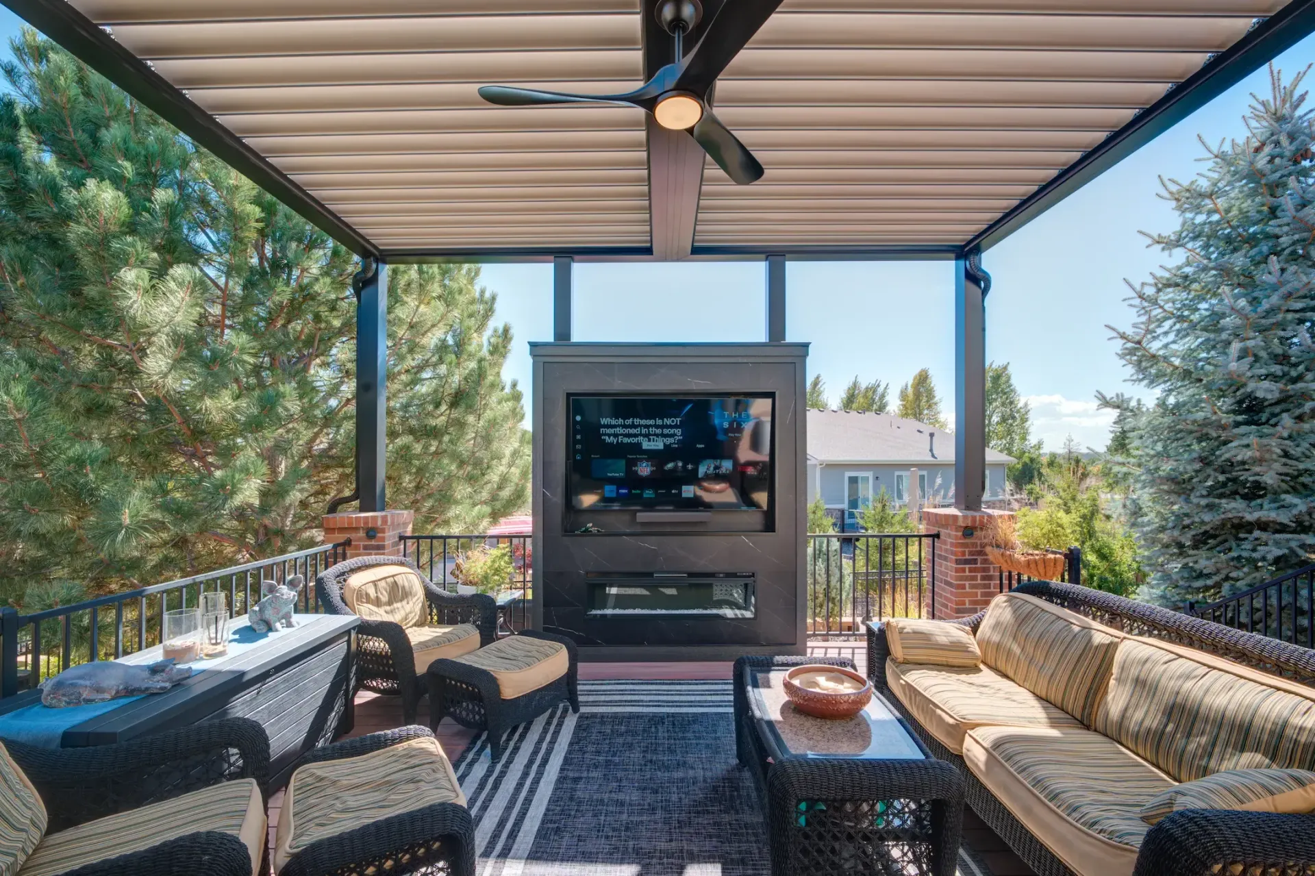 Covered outdoor patio with ceiling fan, fireplace, and seating around a rug and coffee table
