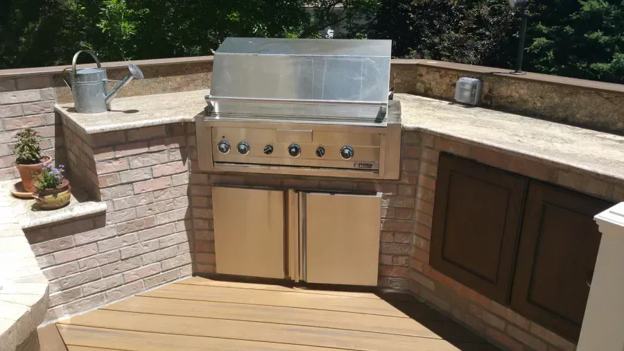 Outdoor built-in stainless steel grill with stone countertop and wooden deck seating area