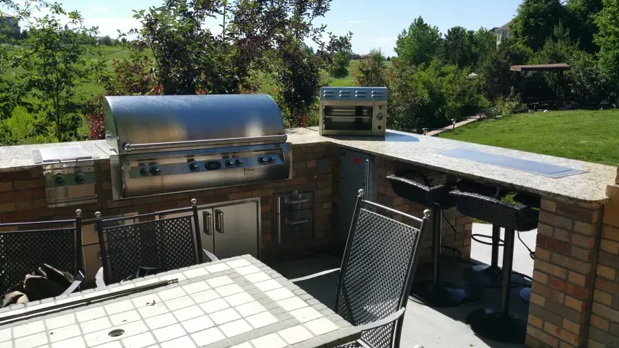 Outdoor patio with brick barbecues, metal chairs, and a table overlooking trees.