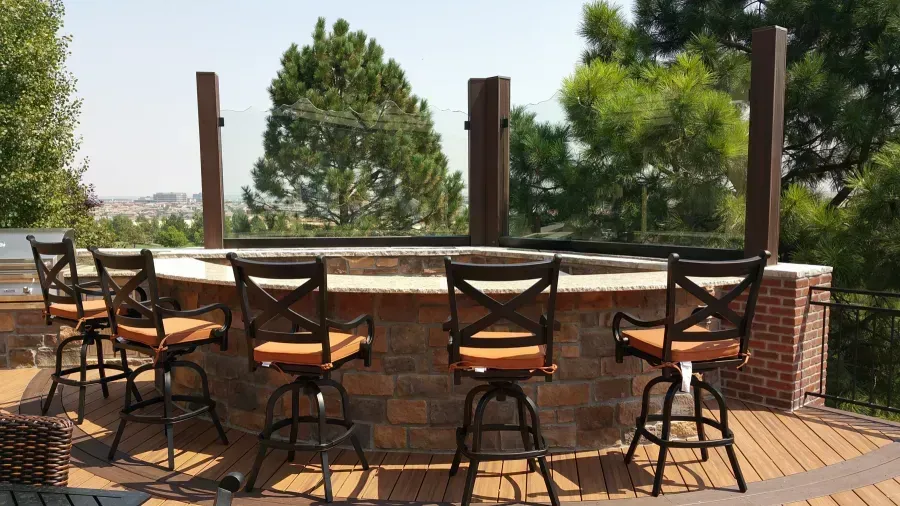Outdoor patio with a round bar, black chairs, brick columns, and trees in the background