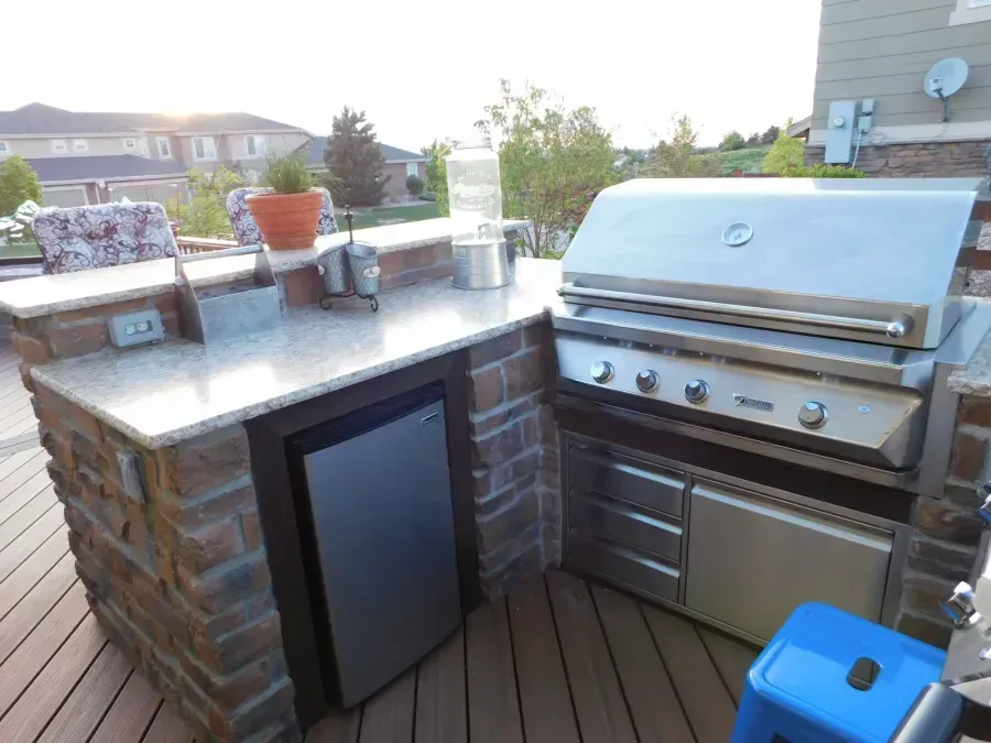 Outdoor patio with stainless steel grill, stone counter, mini fridge, and wooden deck seating area