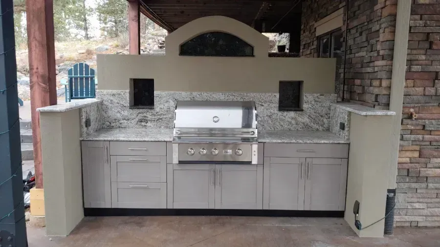 Outdoor built-in grill station with gray cabinets, granite counter, and stone backsplash under a covered patio