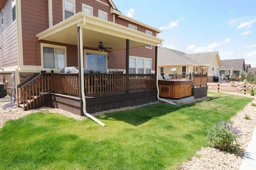 Backyard deck with wooden railing, white columns, and a small hot tub beside a brick house.