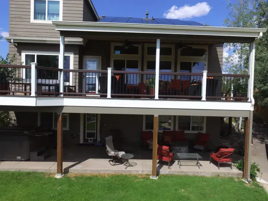 Two-story house with covered porches, white railings, and outdoor chairs on the lower patio.