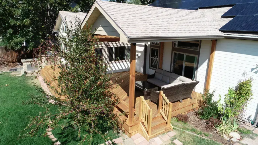 Backyard patio with wooden steps, covered seating area, and green lawn beside a house