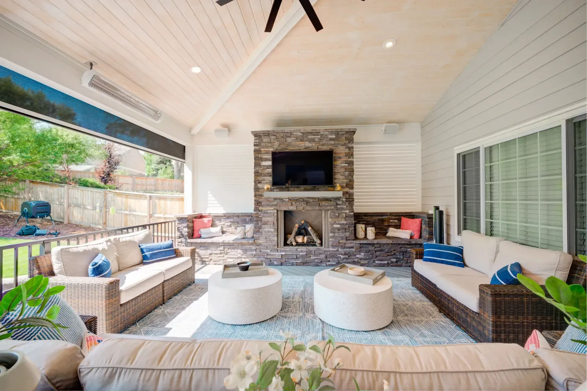 Covered patio with wicker seating, round ottomans, and a stone fireplace under a white ceiling