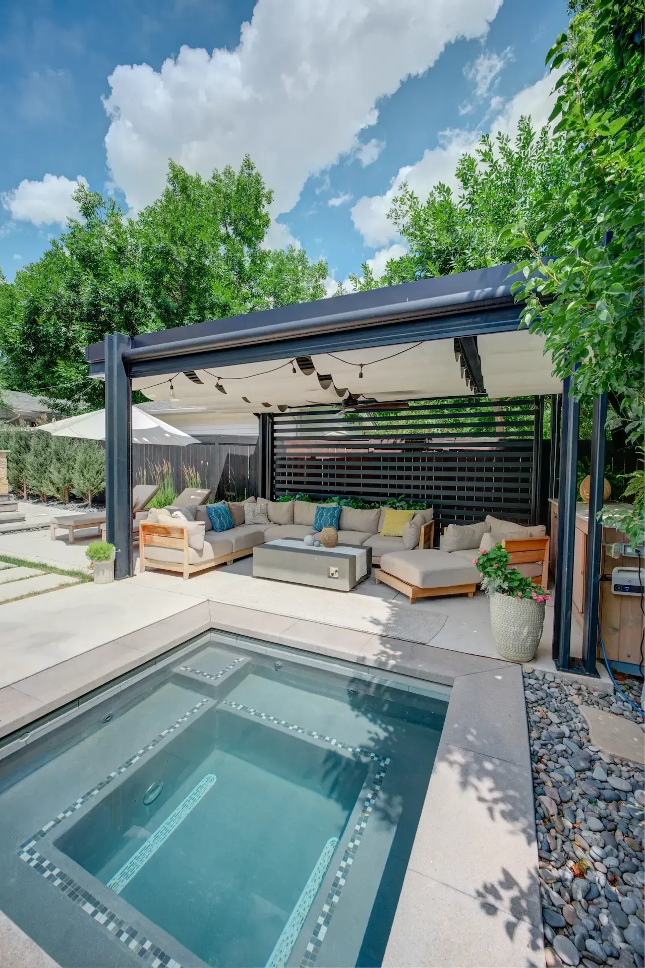 Modern patio with covered lounge seating beside a small rectangular pool under a blue sky
