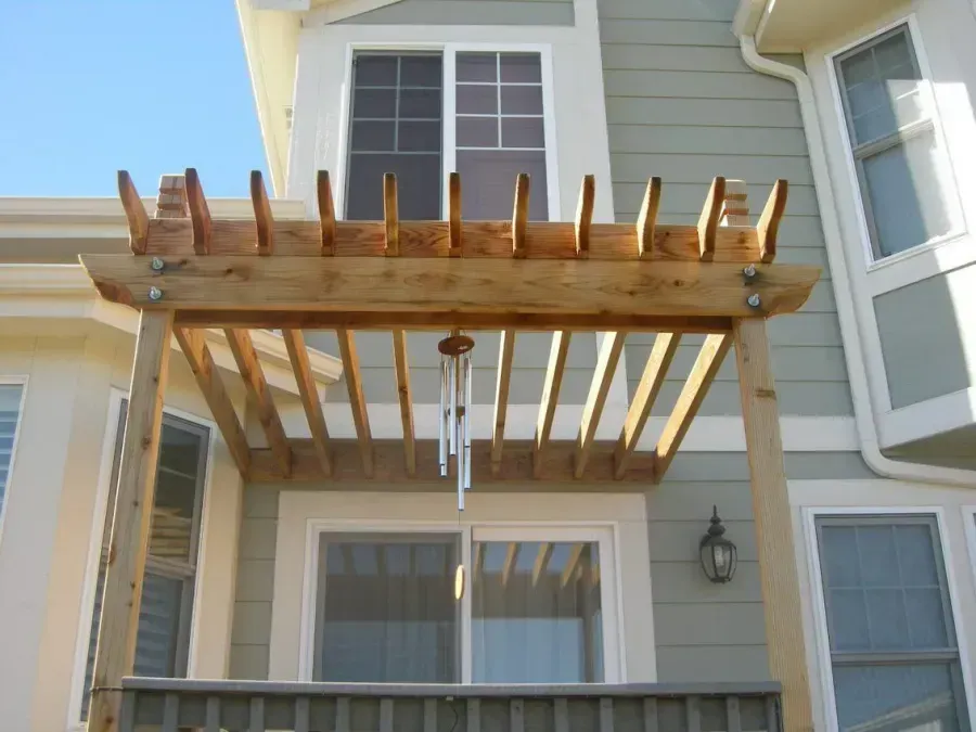 Wooden deck pergola attached to a beige house with white-trimmed windows and hanging icicles