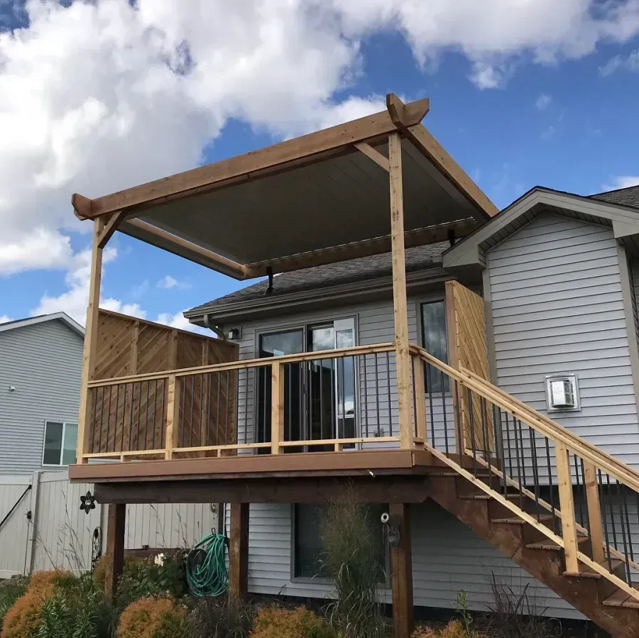 Raised wooden deck with stairs and a covered patio attached to a gray house under a cloudy sky