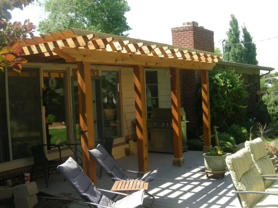 Wooden patio pergola with striped shadows over lounge chairs in a sunny garden