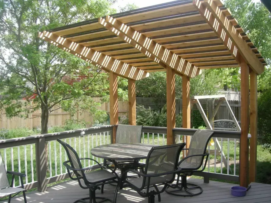 Backyard patio with wooden pergola, black metal table and chairs, and a grill