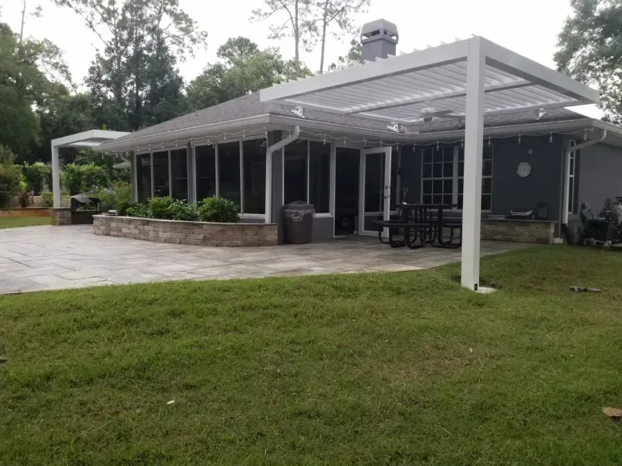 Modern house with a covered patio, large windows, stone planter, and grassy yard.