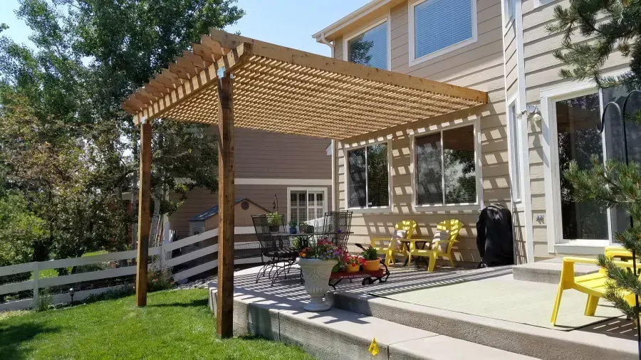 Backyard patio with wooden pergola, yellow chairs, and steps beside a house