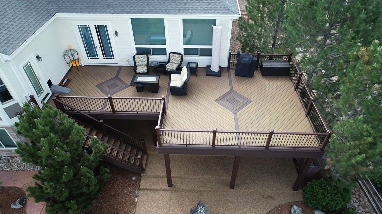 Backyard deck with outdoor seating, railing, and stairs beside a house and trees.