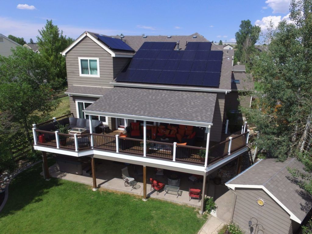 Suburban house with solar panels and a large covered deck, surrounded by trees and lawn