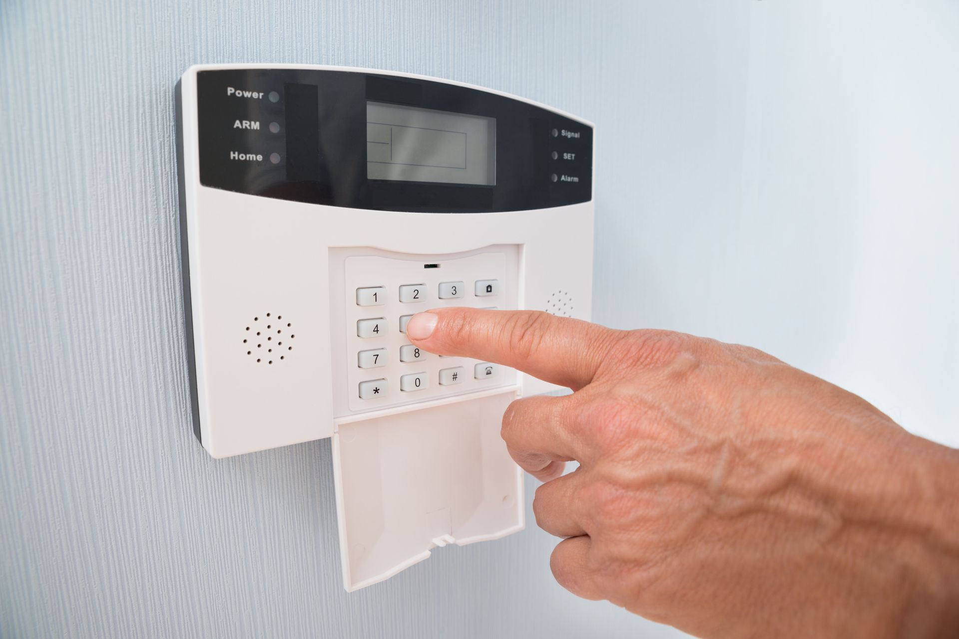 Hand entering code on a white home security system keypad mounted on a blue wall.