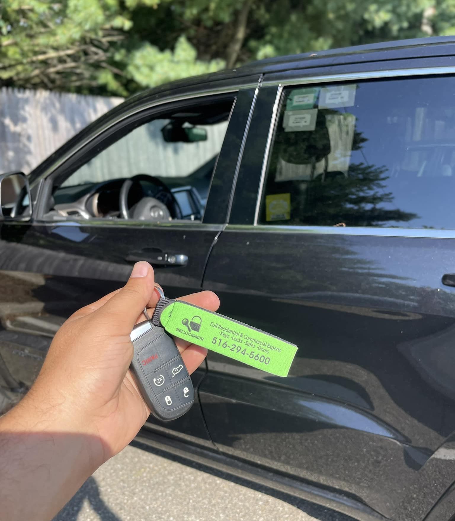 Hand holding car key with green tag next to dark gray SUV.