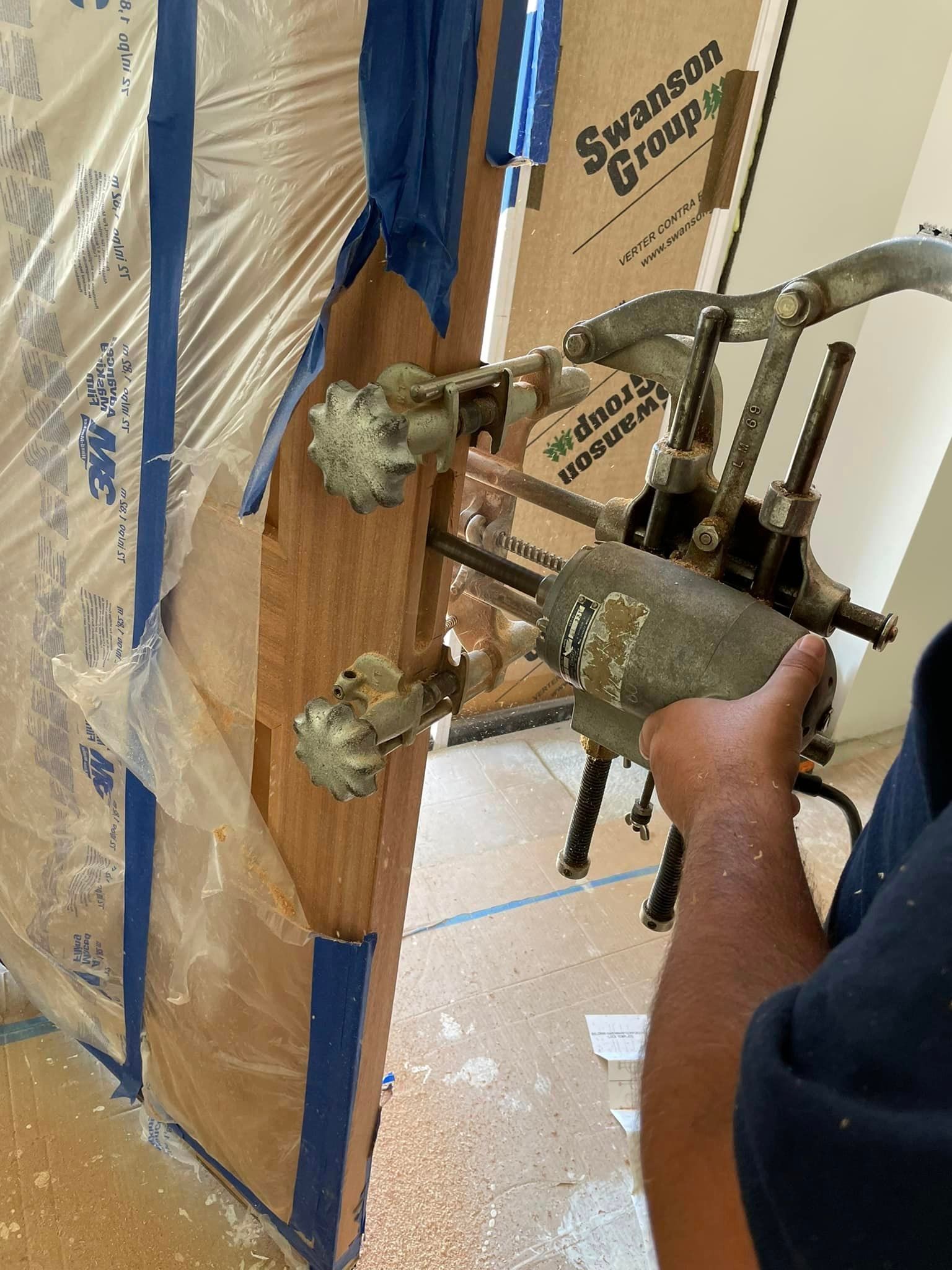 Person using a tool to work on a wooden door. The tool has several nozzles attached to the door.