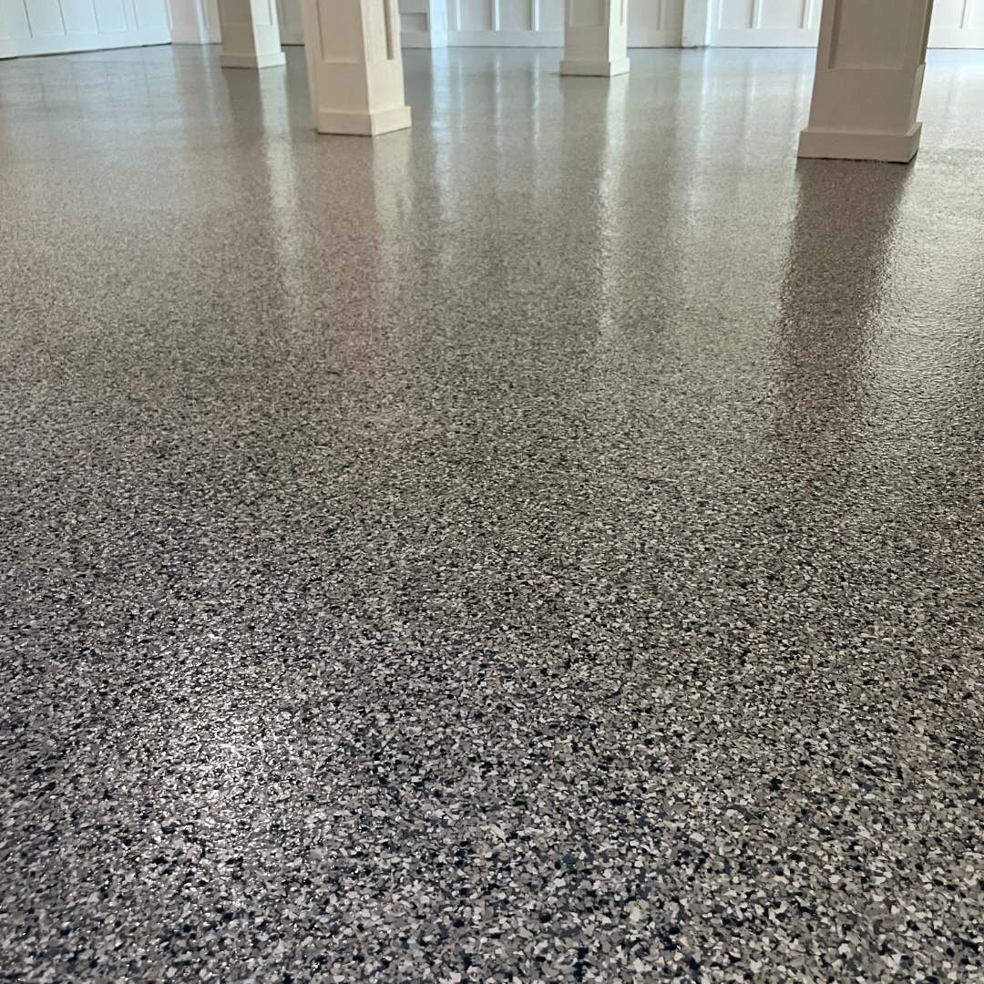 Garage with a speckled epoxy floor. A black tarp and paint can are in the foreground. Gray walls and trim.