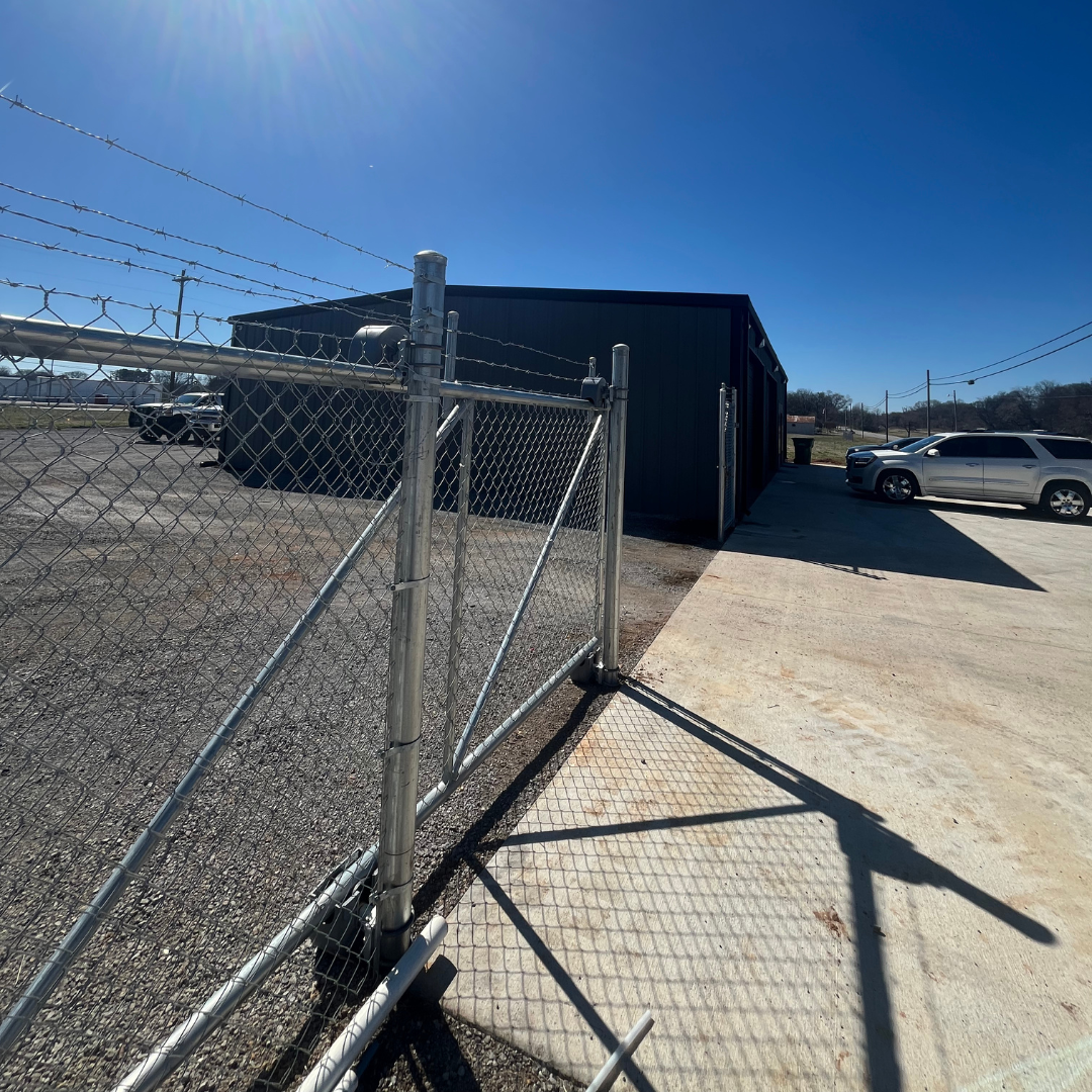 Black fenced-in pool in front of a white house on a sunny day.