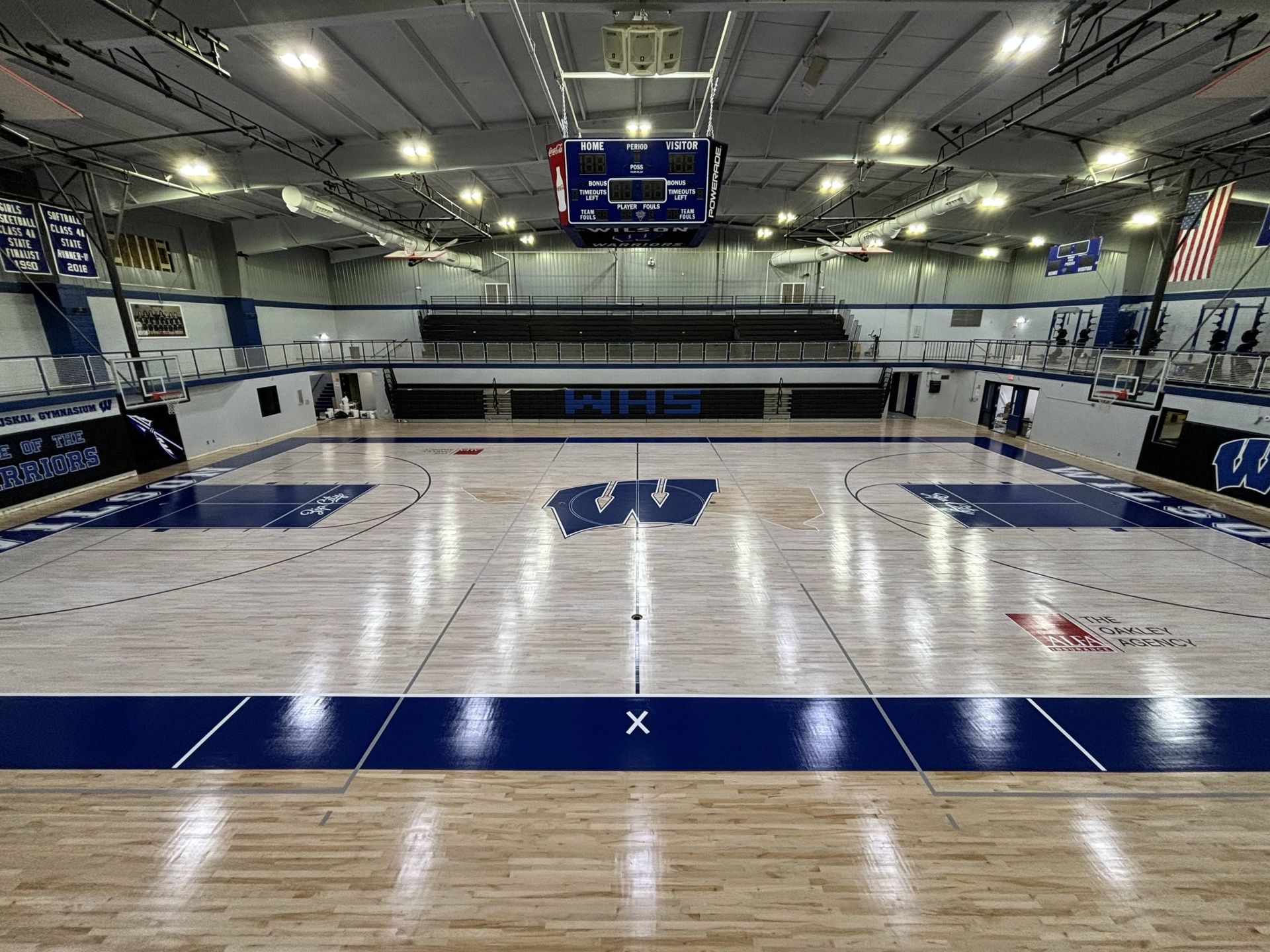 Basketball court with wood floor and blue trim; scoreboard overhead.