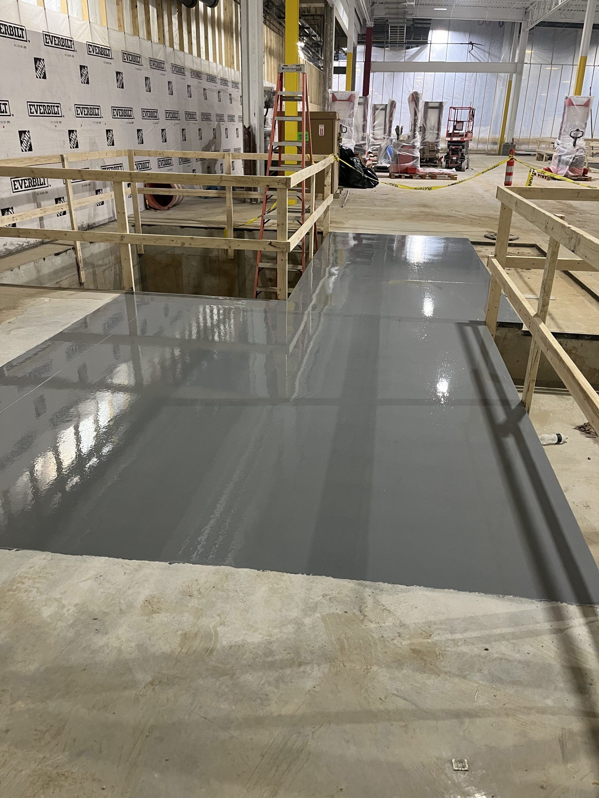 A newly painted gray concrete floor in a construction setting. Wooden safety rails line the edges.