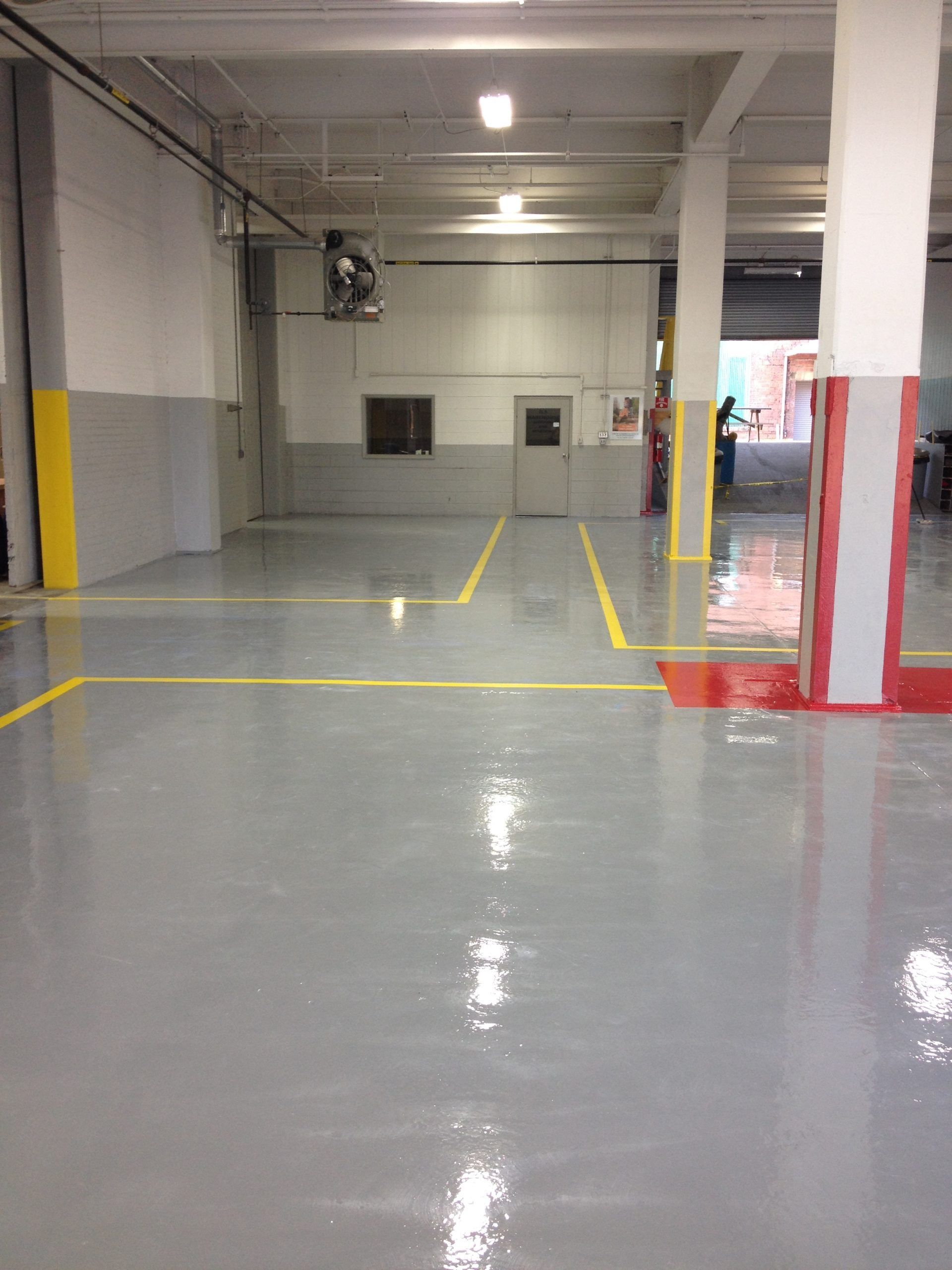 Grey concrete floor with yellow lines, white and grey walls, and structural columns.
