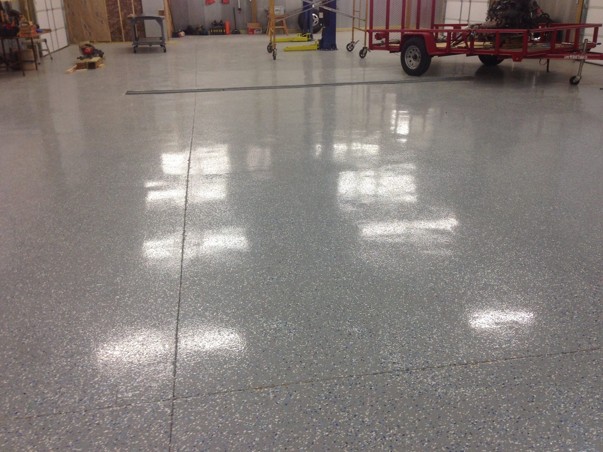 Grey speckled epoxy floor with cracks, reflecting light. A trailer and equipment are in the background.