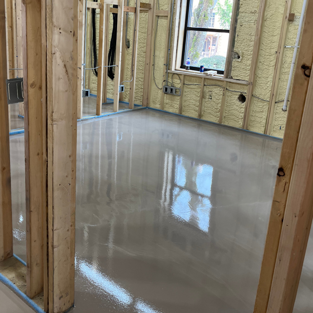 Black epoxy floor reflecting light in an empty room with white baseboards and light gray walls.