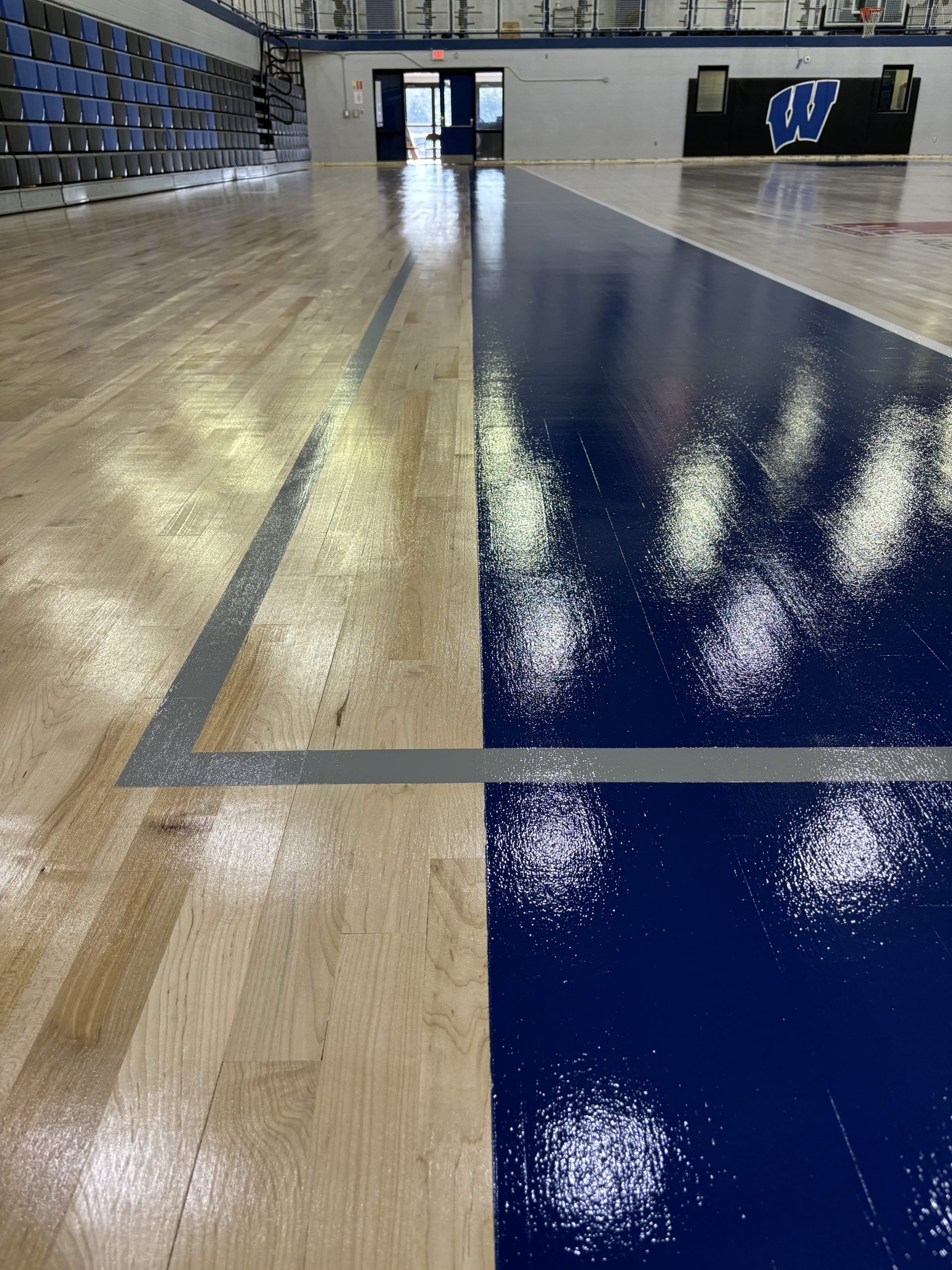 Newly refinished basketball court, half painted blue, half natural wood, with gray lines.