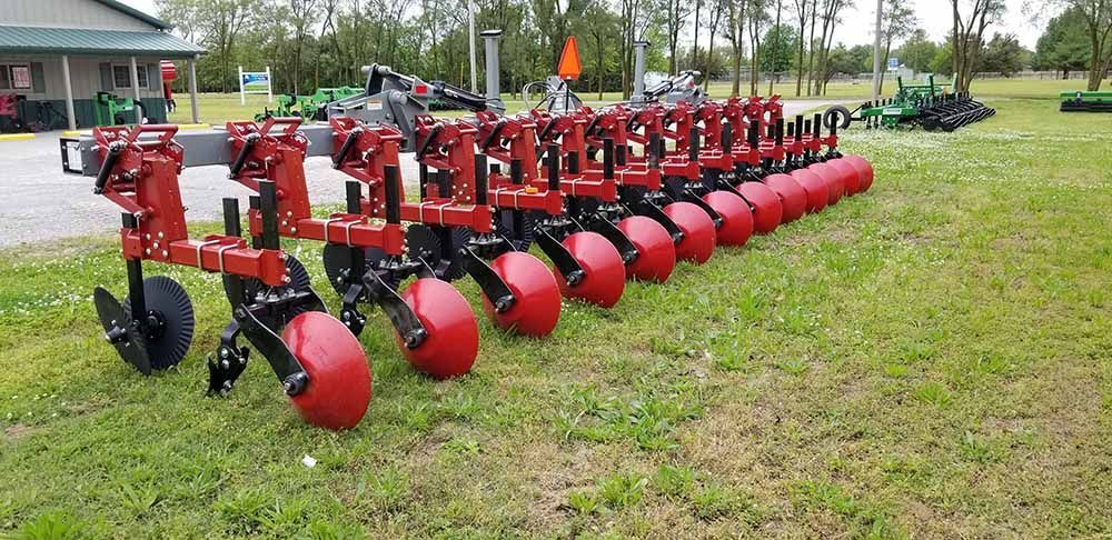A row of red tractors are parked in a grassy field.