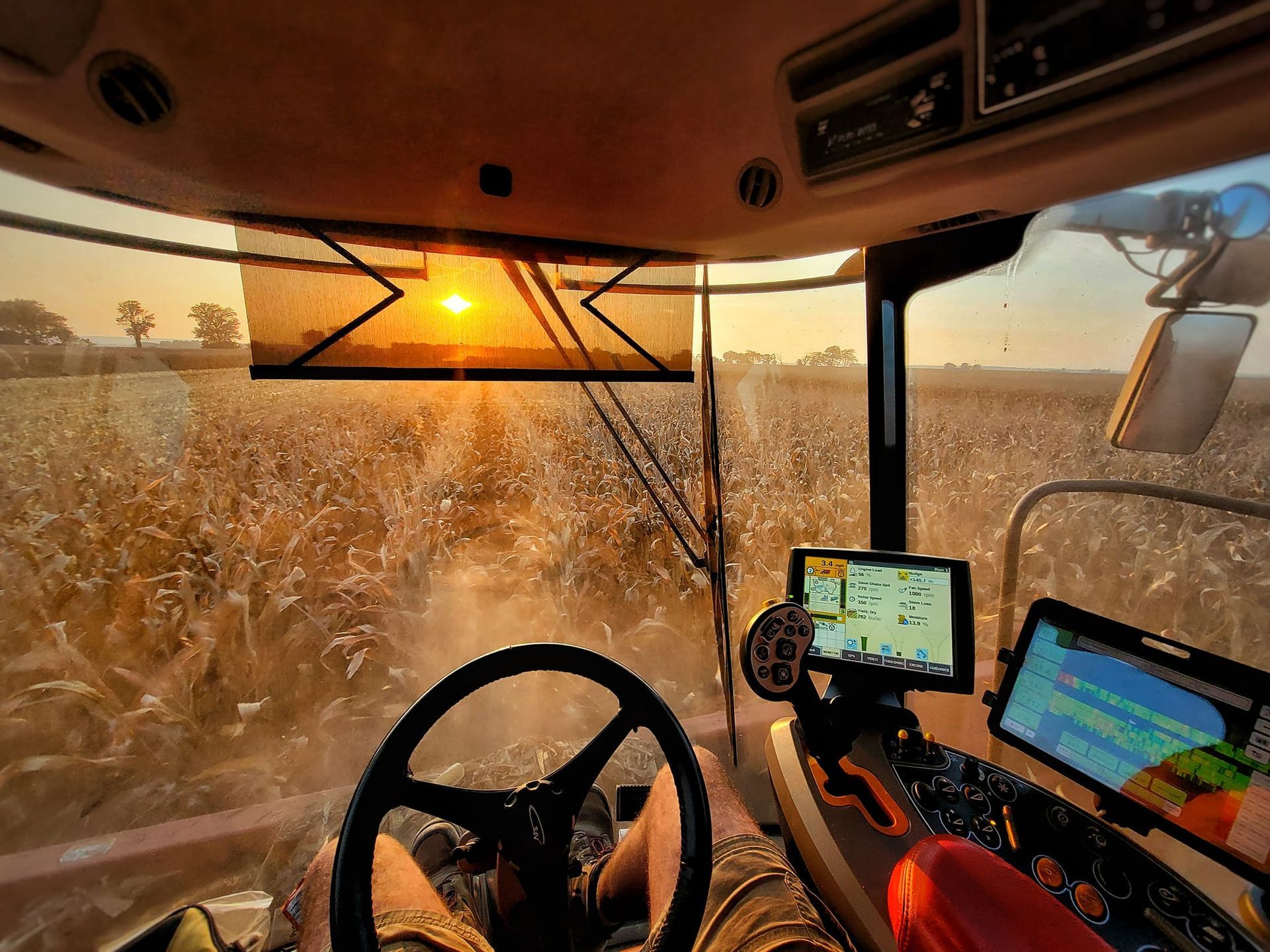 A person is driving a tractor in a field at sunset.