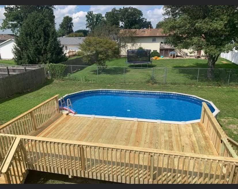 Wooden deck with brown composite planks, overlooking a grassy field and trees under a blue sky.