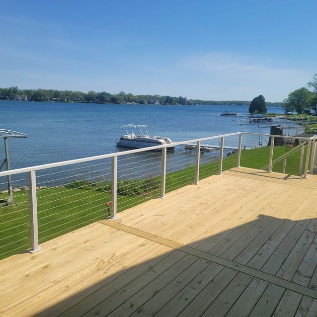 Wooden deck overlooking a lake with boats, blue sky, and green grass.