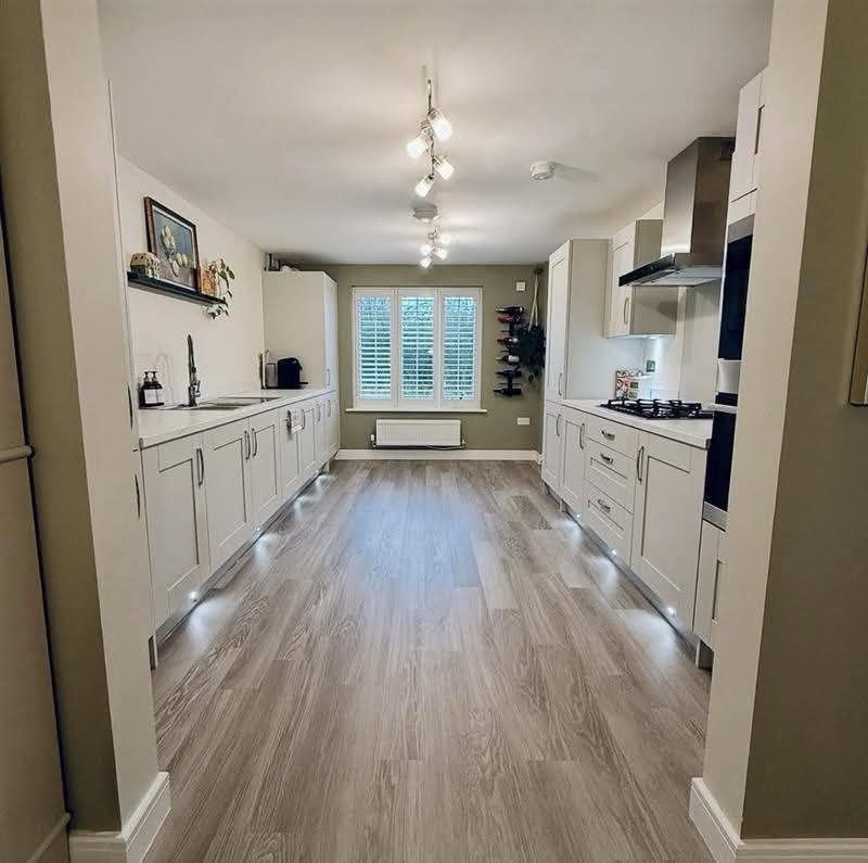 Modern kitchen with light cabinets, light wood-look floor, centered lighting, and a window with shutters.