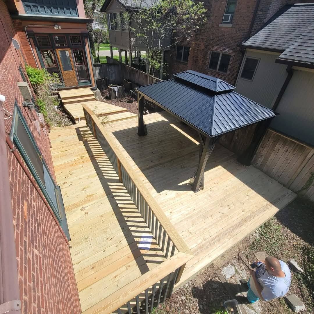 Wooden deck with gazebo and railing, next to a brick building. Person painting near edge.