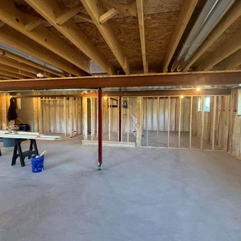 Basement under construction: wood framing, steel beam, support pole, concrete floor.