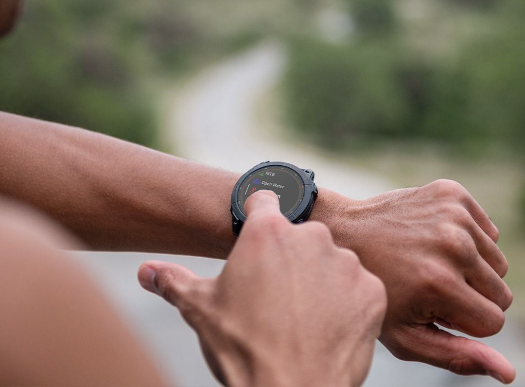 Person using a smartwatch outdoors, touching the screen with their finger, blurred background.