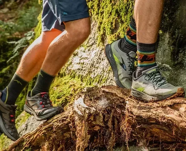 Two runners on a tree trunk in a forest. One wears gray shoes and patterned socks.