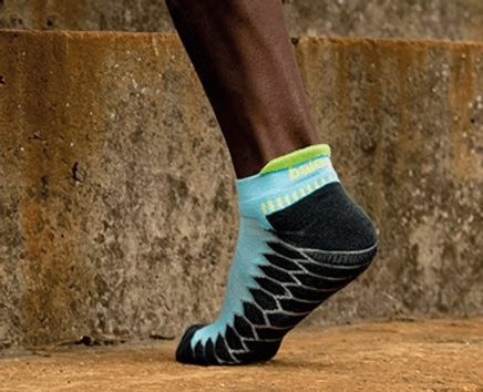 Black ankle in light blue and black athletic sock stepping on concrete stairs.